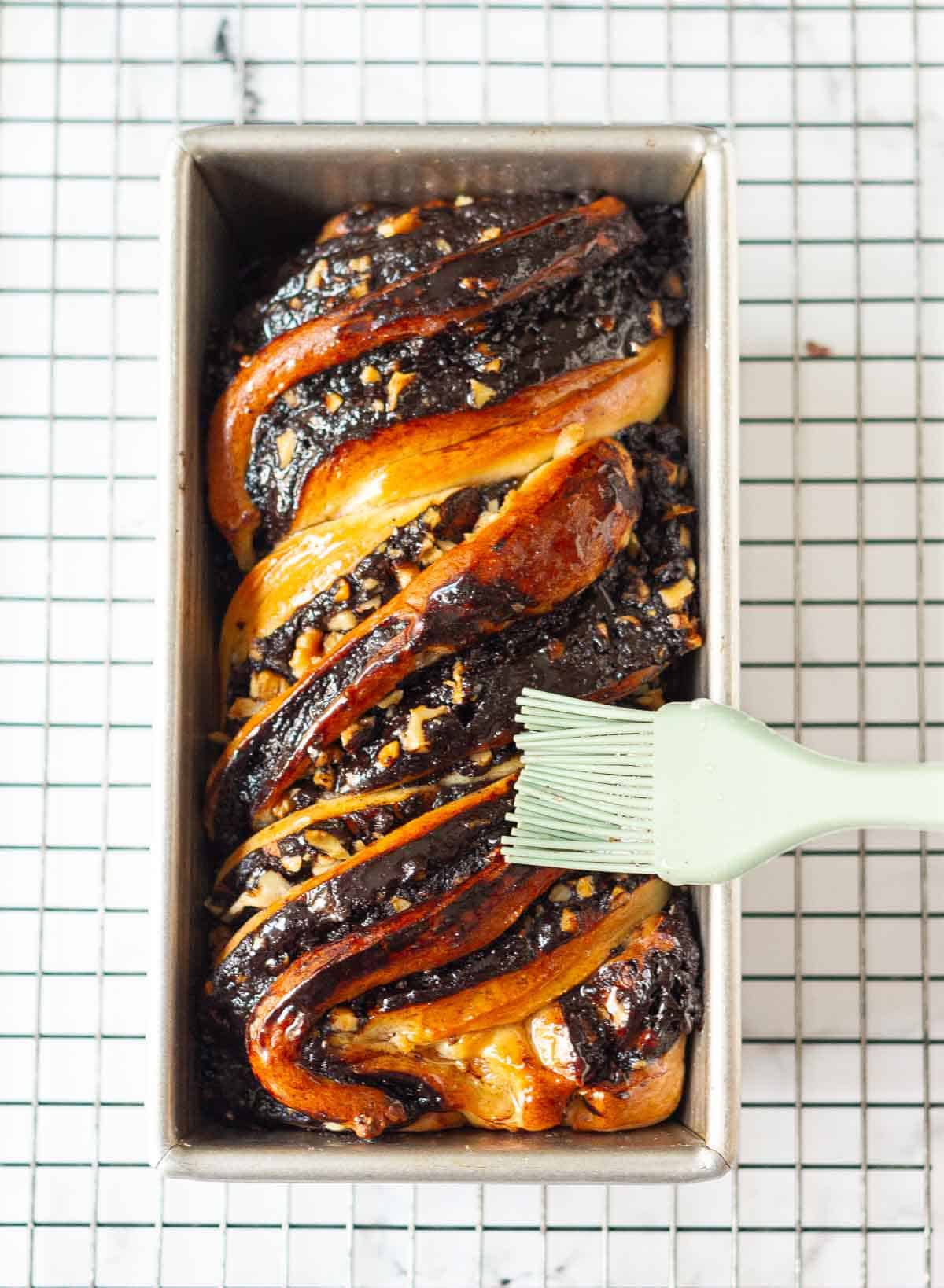 chocolate babka getting brushed with sugar syrup with a pastry brush.