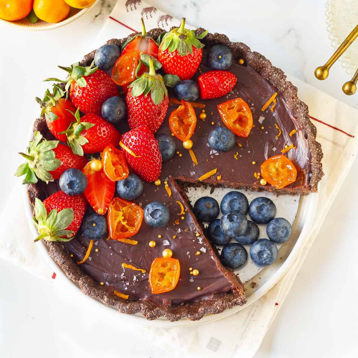 chocolate tart with berries, candied oranges with one slice taken out on a plate.