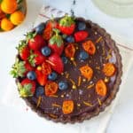 chocolate orange tart garnished with berries, orange zest, candied oranges on a white napkin.