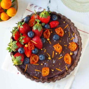 chocolate orange tart garnished with berries, orange zest, candied oranges on a white napkin.