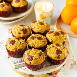 Muffins topped with chocolate chips on a white tray with a candle and oranges around.