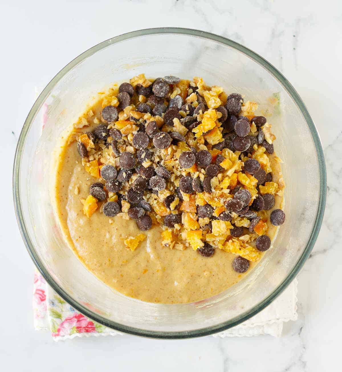 Chopped walnuts, chocolate chips, and candied oranges on top of batter in a bowl.
