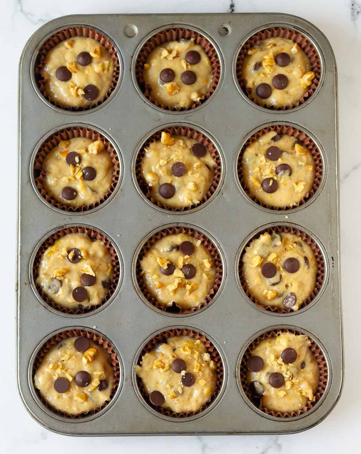 Muffin batter in a muffin tray topped with chocolate chips.