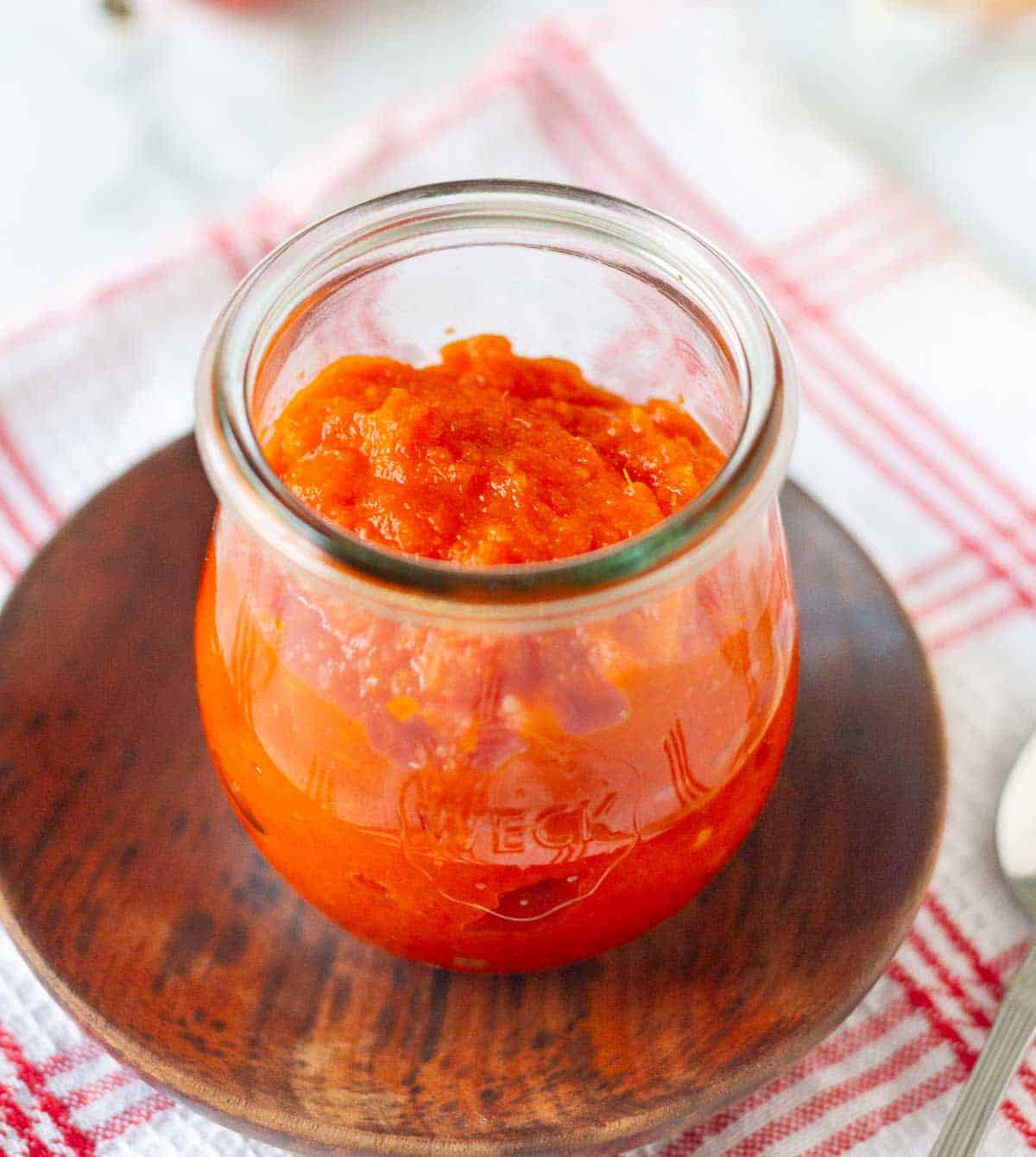 Cooked chili sauce in a glass jar on a small plate.