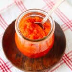 Sambal Oelek sauce in a glass jar with a spoon on a wooden plate.