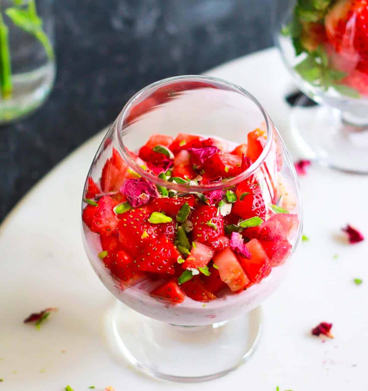 chia pudding with strawberry, pistachio, and rose petal toppings in a dessert glass.