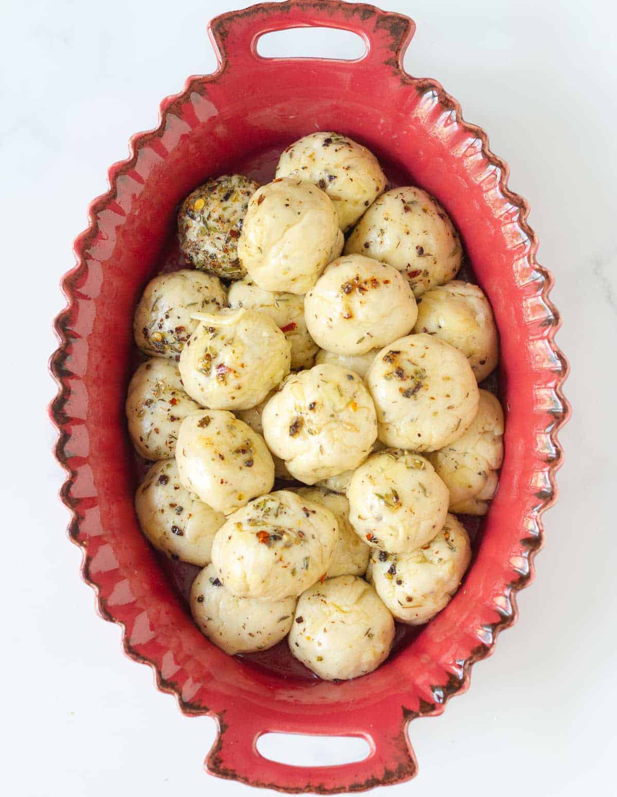 Bread dough balls in a red baking dish.