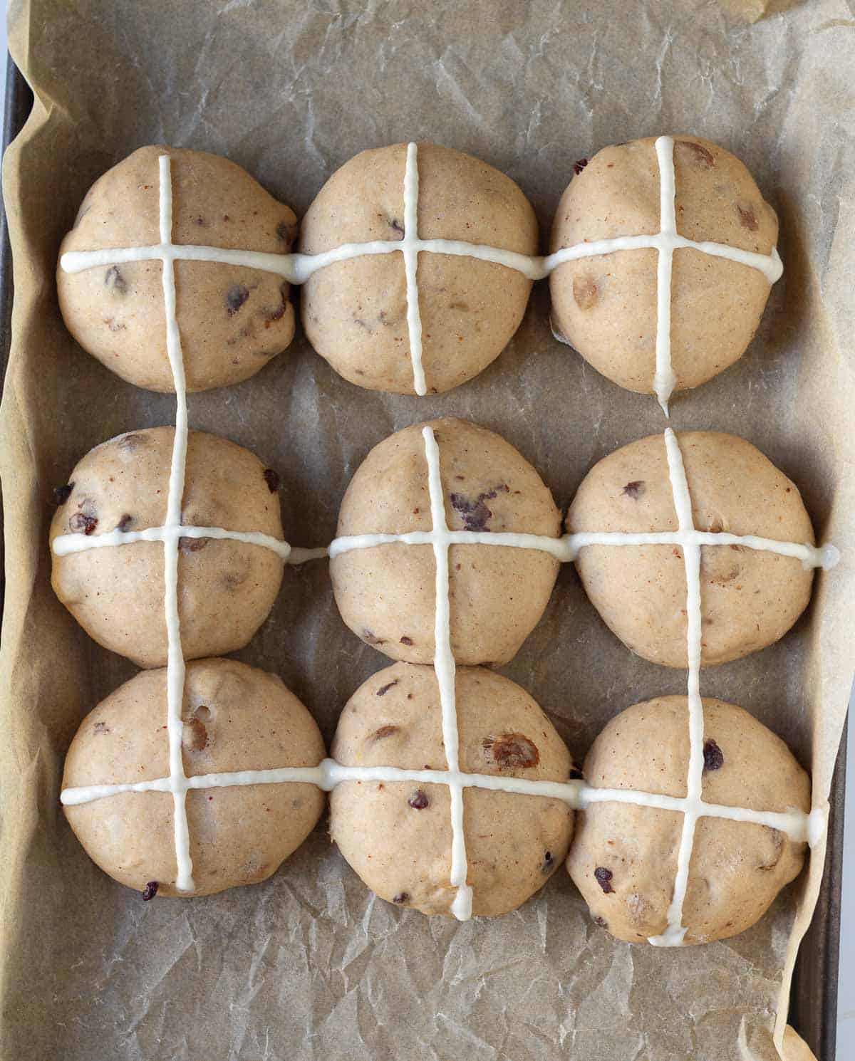 9 dough balls marked with a flour paste cross on a parchment paper lined tray.