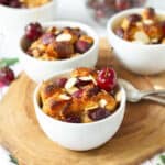 cherry bread pudding in 3 ramekins with spoons on the side on a wooden board.