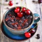 Chocolate cherry mug cake in a blue cup, topped with fresh cherries and chocolate.