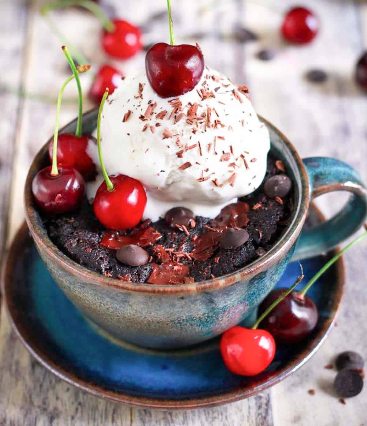 Mug cake with a scoop of vanilla ice cream and fresh cherries on top.