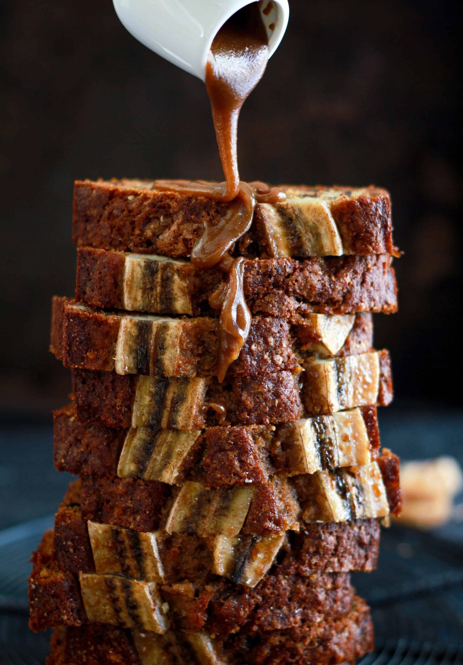 Stacked slices of Walnut & Fig Banana Bread with caramel sauce.