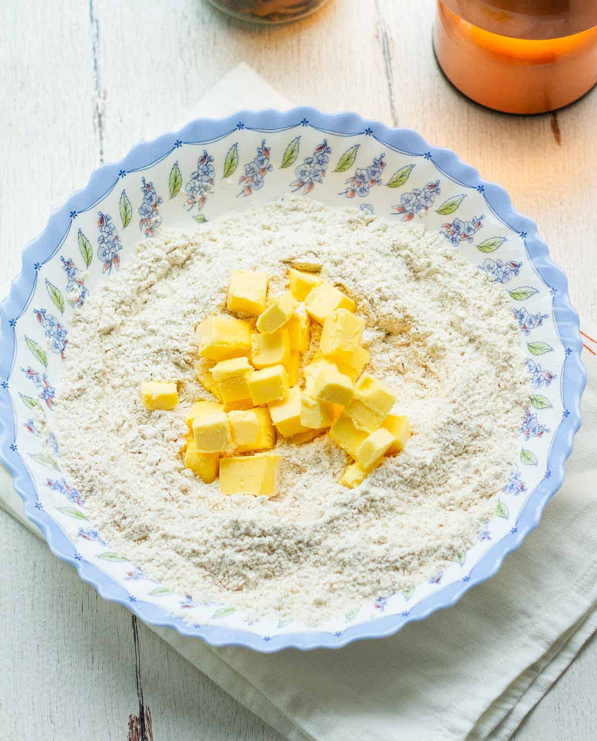 Butter cubes on top of dry ingredients in a blue bowl.