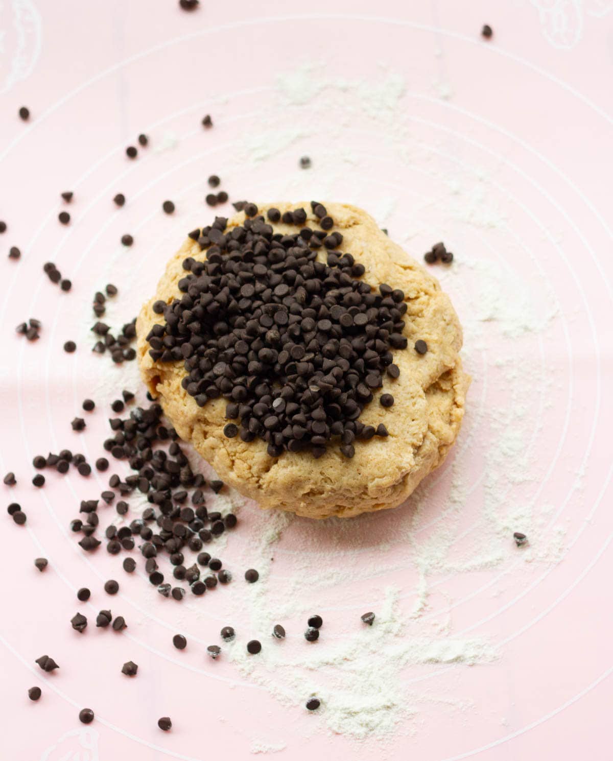 Chocolate chips on top of dough on a silicone mat.