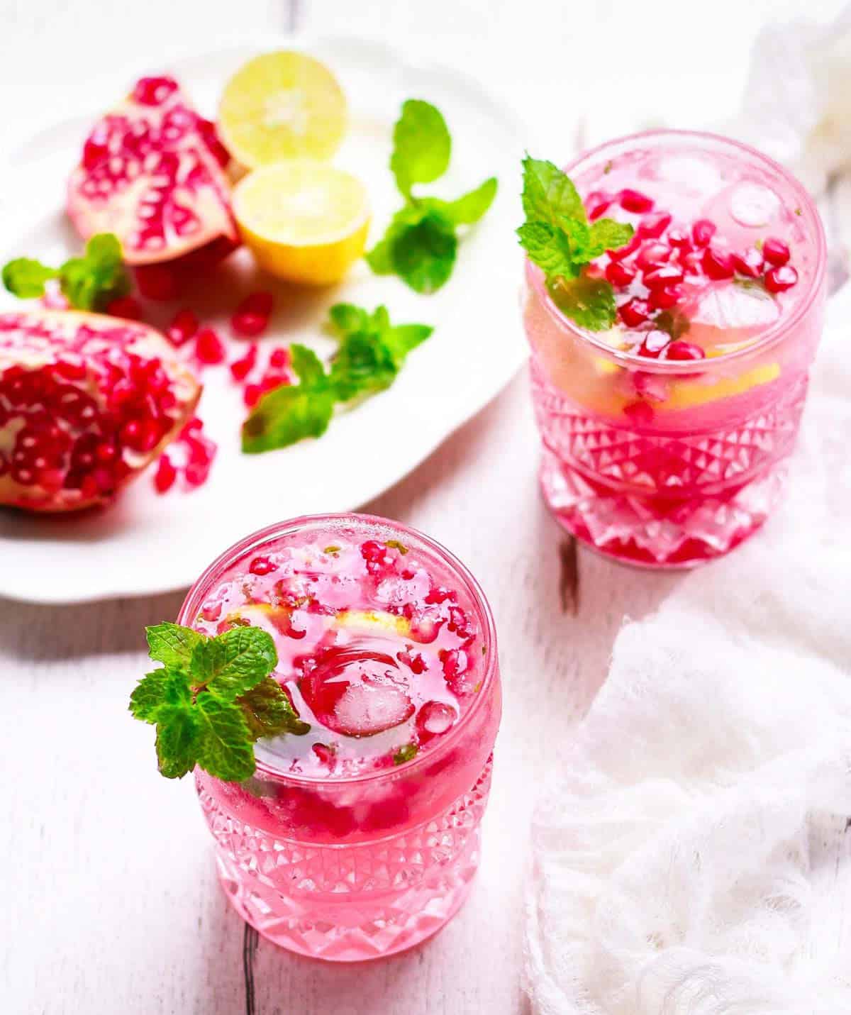 Pomegranate mojito in 2 glasses with ingredients in the background.