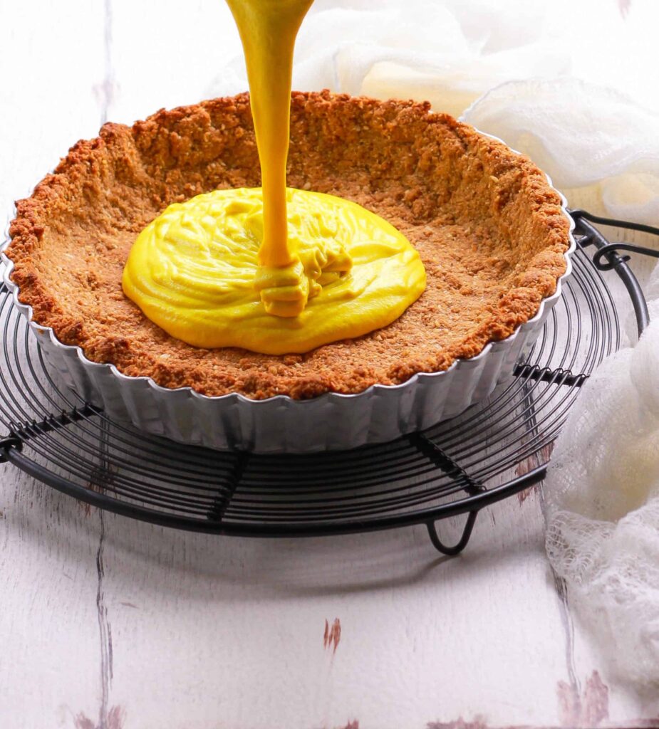 Lemon curd filling being poured in a tart crust.