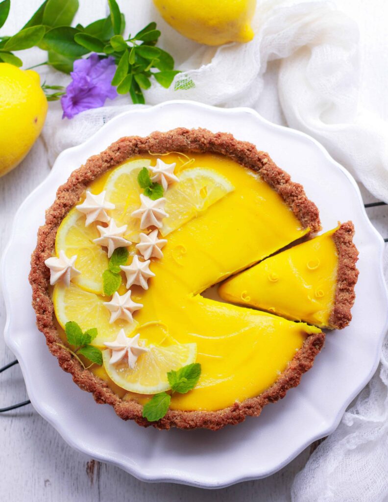 Vegan Lemon Tart with slice cut, decorated with mint and meringues.