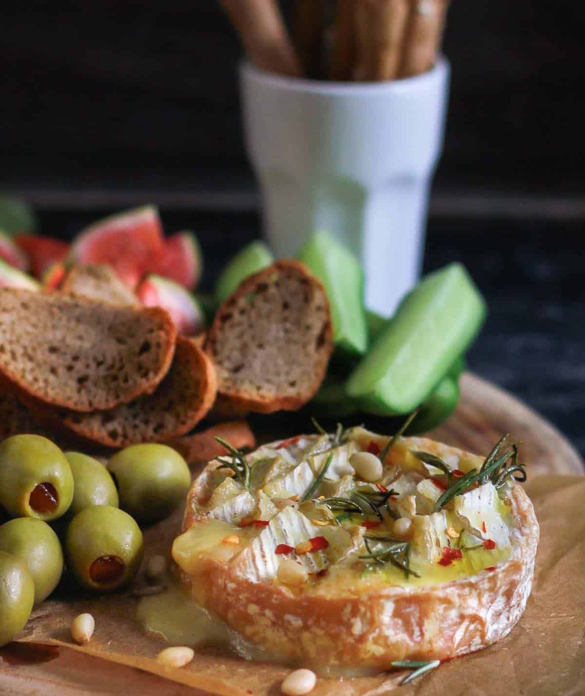 camembert with crackers, olives, cucumbers on a wooden board.