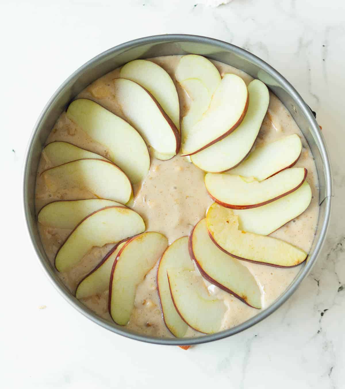 Cake batter topped with apple slices in a cake tin.