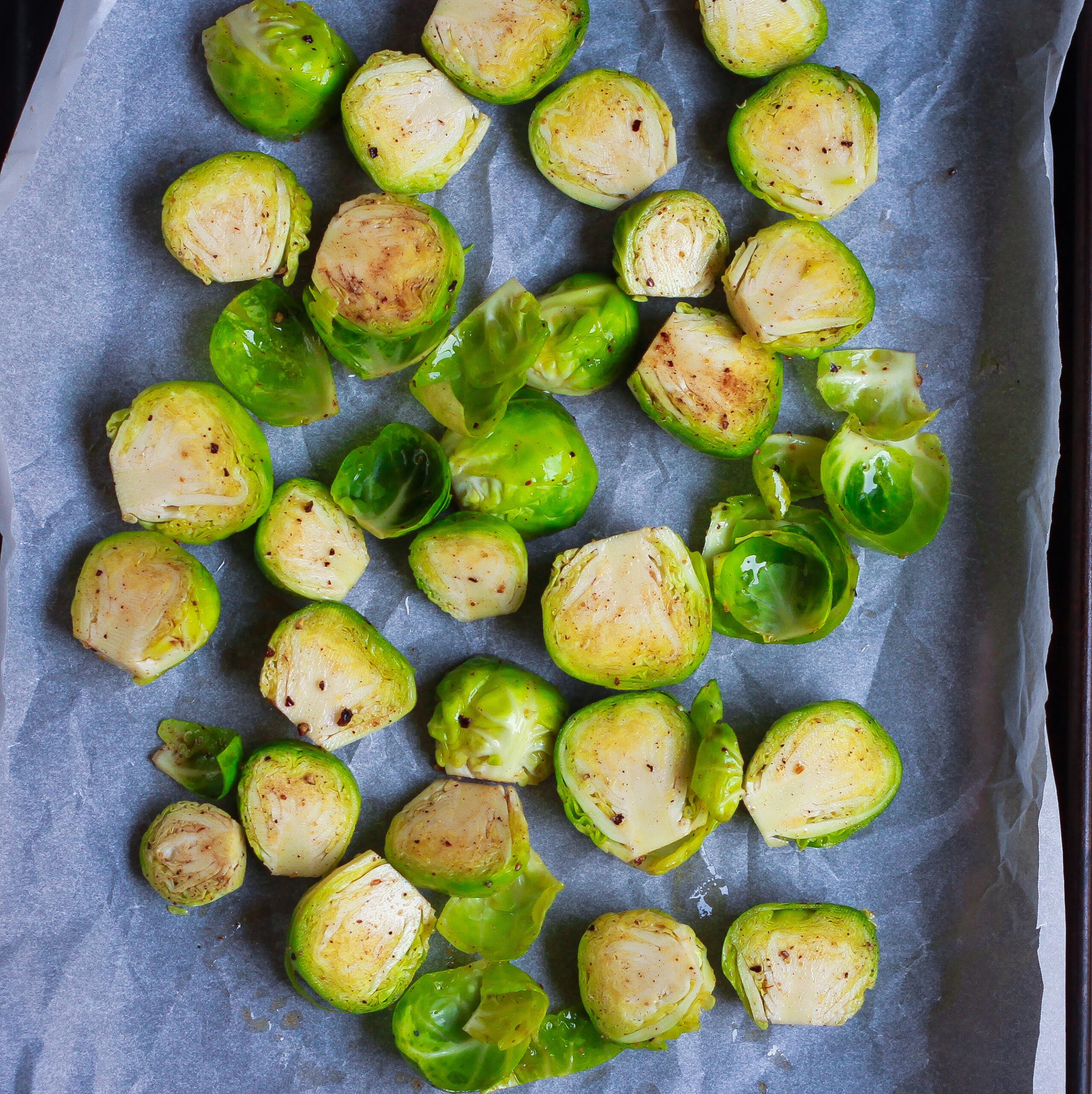 Brussels sprouts coated in spices and olive oil on a parchment-lined tray.