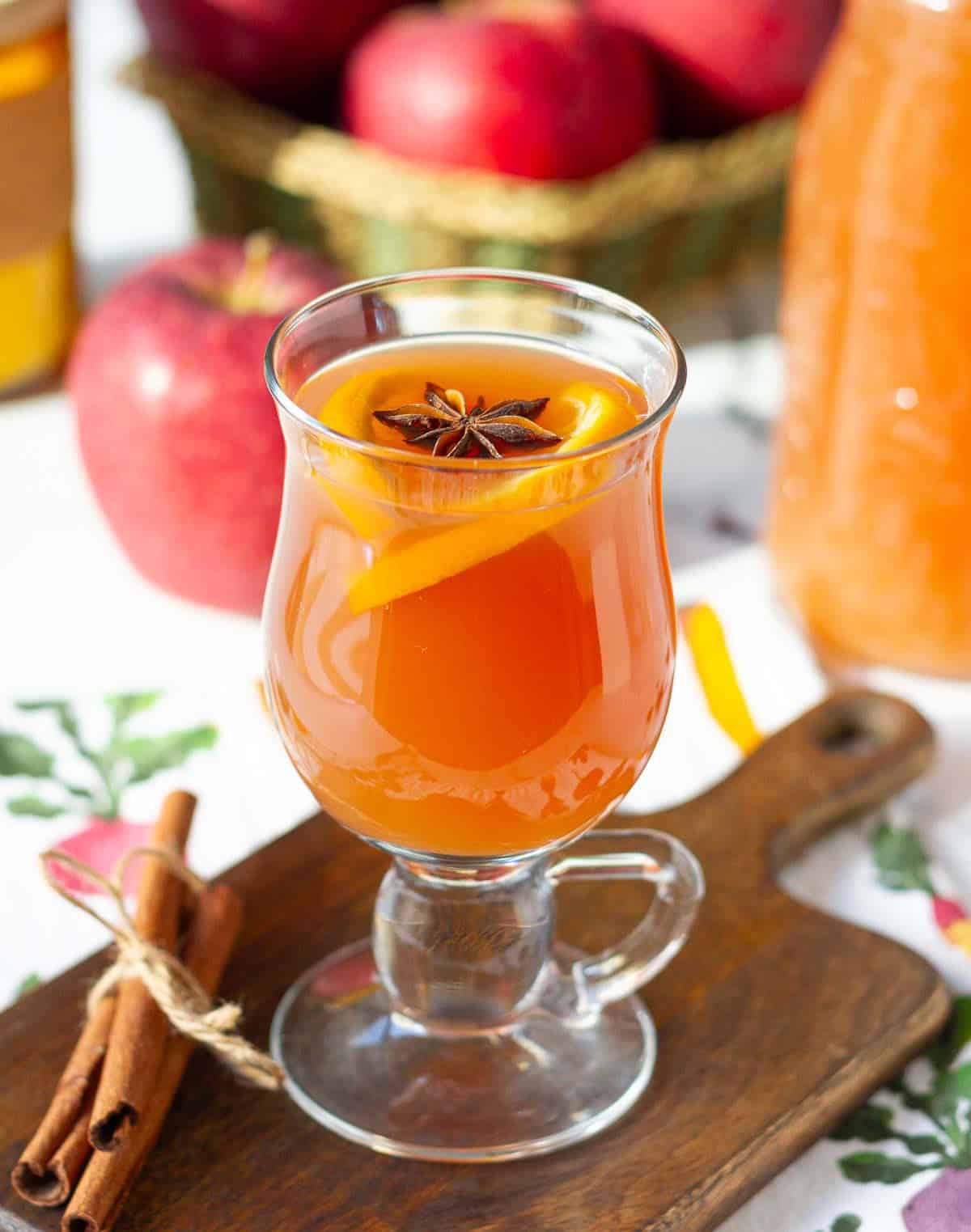 Apple cider in a glass on a wooden board with ingredients in the background.