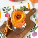 Apple cider in a clear glass garnished with orange slices and star anise.