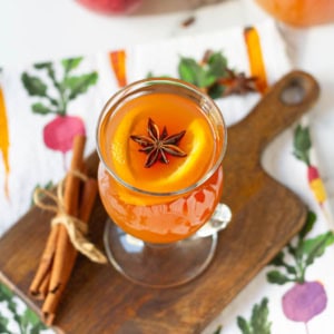 Apple cider in a clear glass garnished with orange slices and star anise.