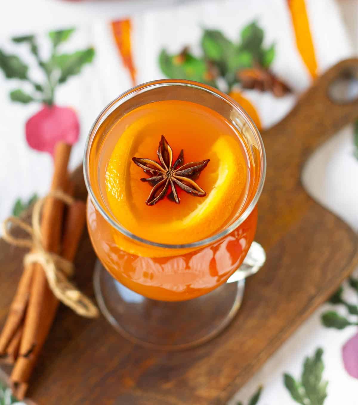 Apple cider in a glass with sliced oranges and star anise on a wooden board.