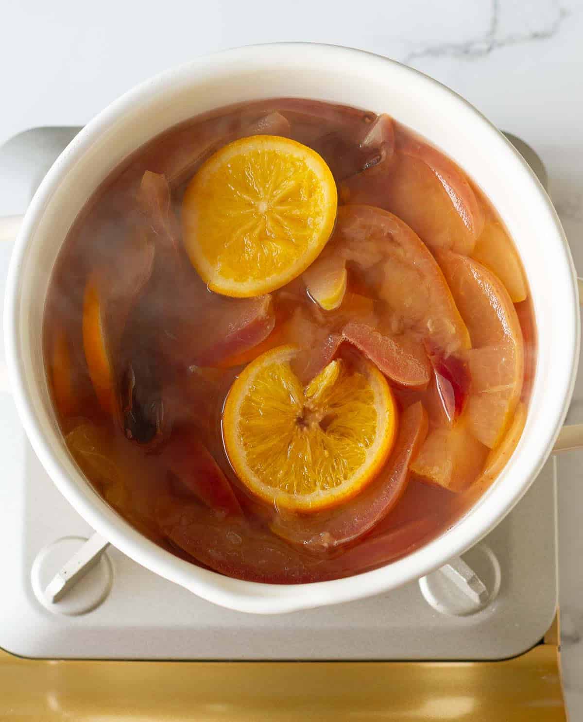 Apples, oranges, spices simmering in a pot.