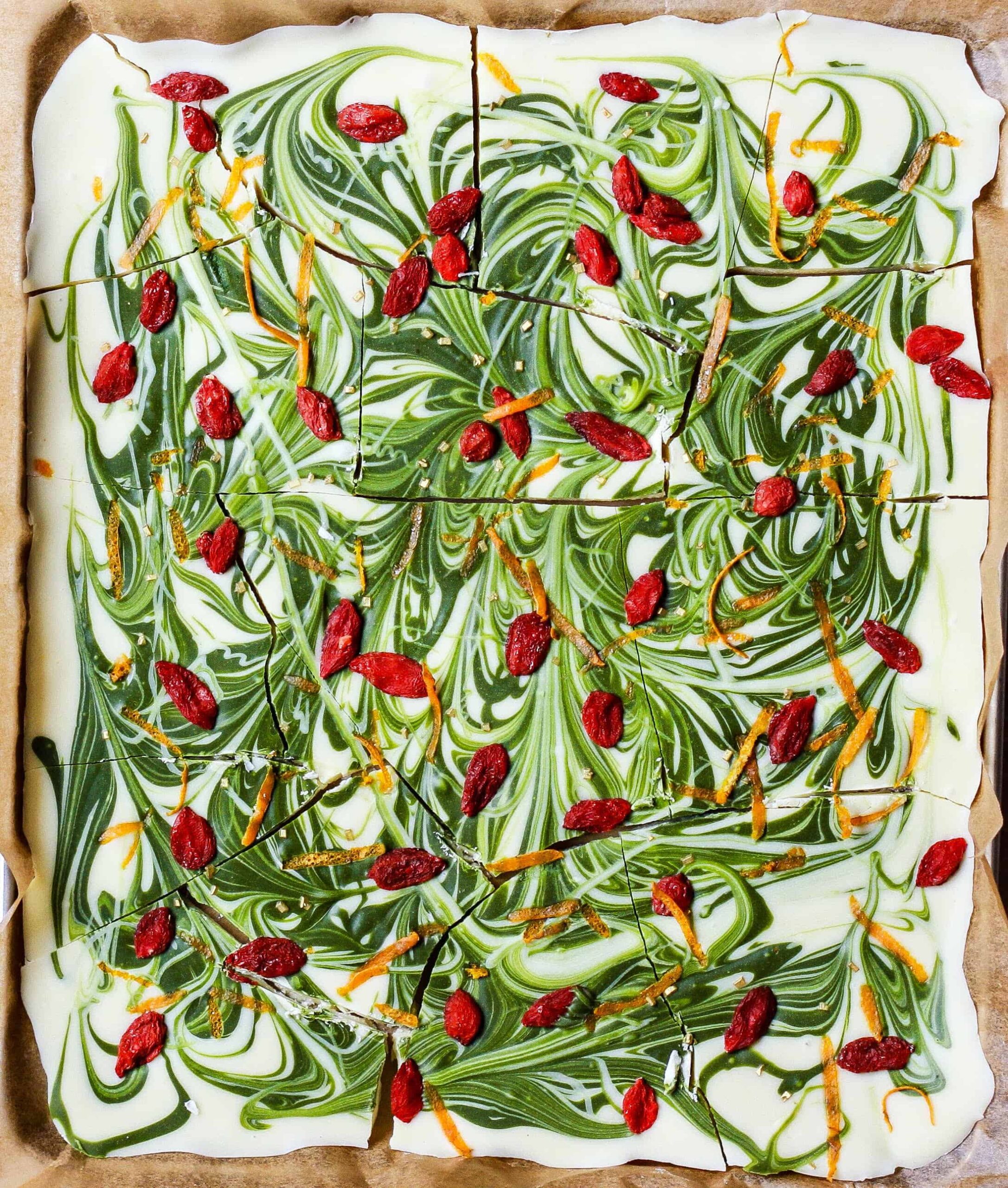 White chocolate bark with matcha swirls and goji berries on parchment paper.