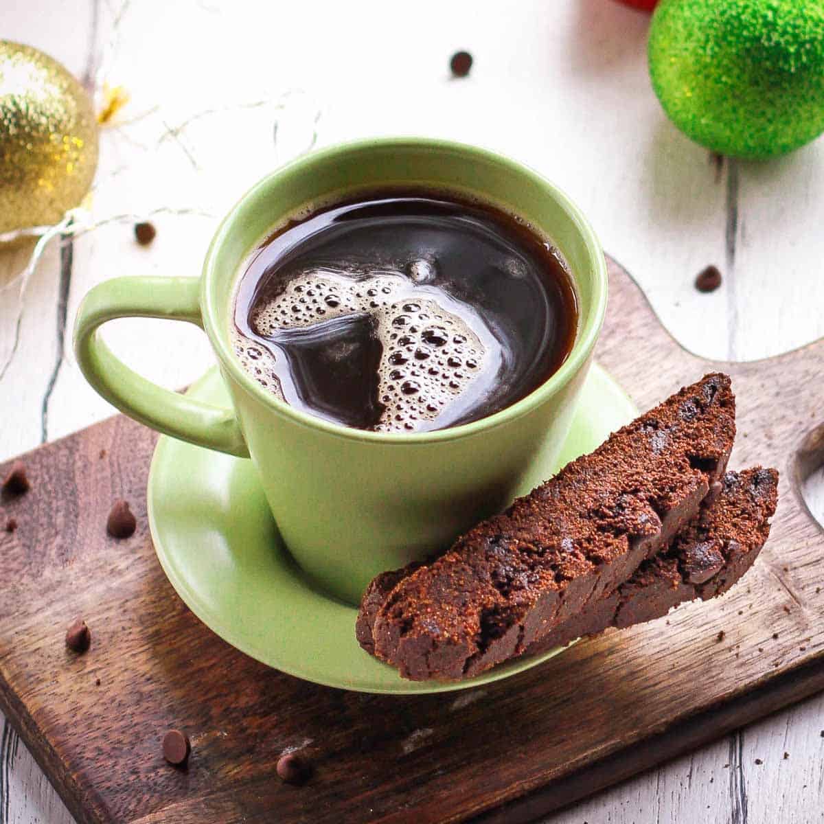 A cup of coffee with 2 biscotti on the saucer.