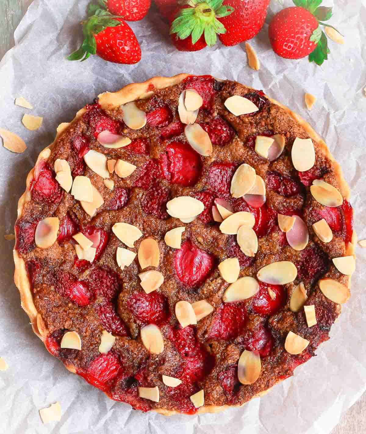 A tart with strawberries and almonds on parchment paper.