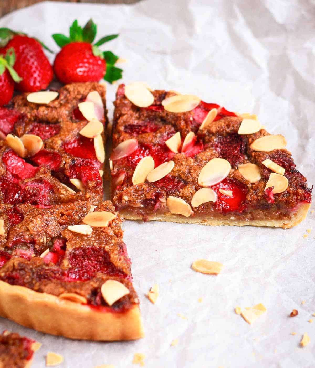 Slices of a pie on white paper with strawberries.