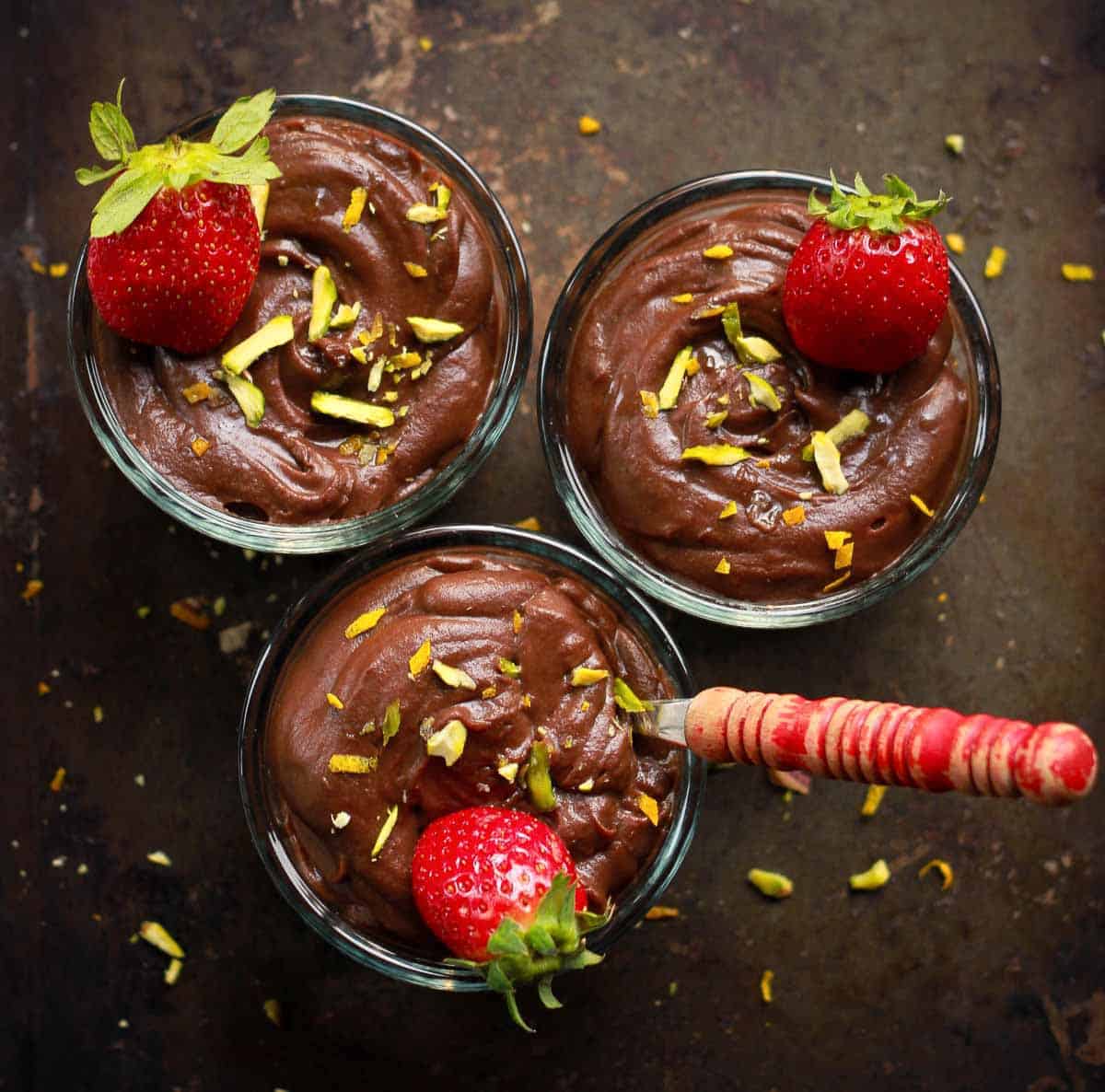 3 bowls of chocolate pudding with strawberries and a spoon.