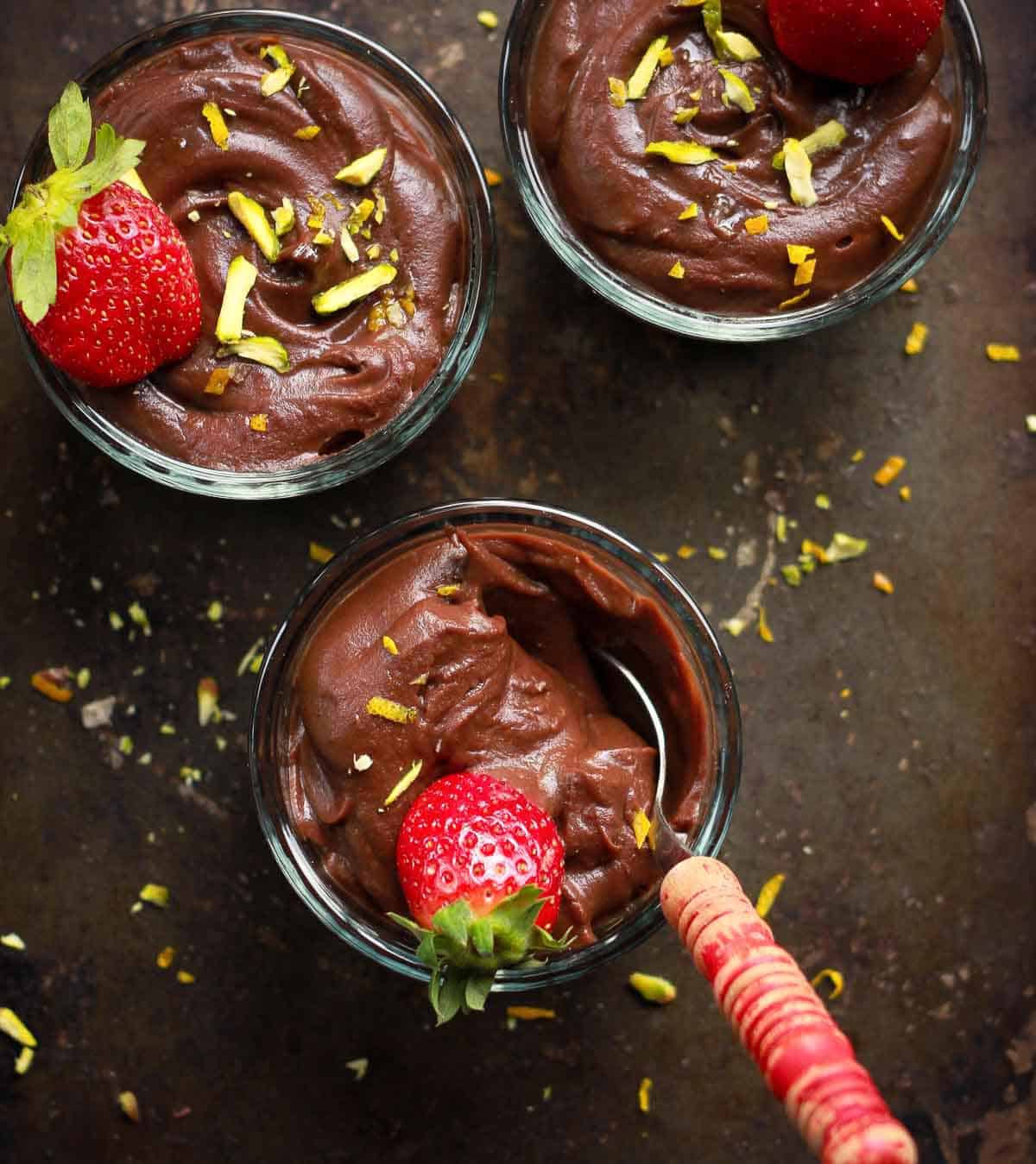 3 bowls of chocolate pudding with a spoon in one bowl.
