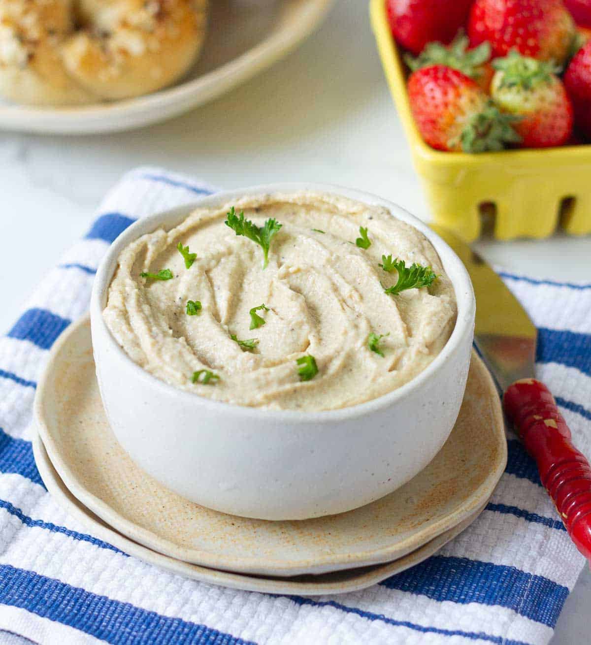 cashew cheese in a bowl with strawberries and bagels in the background.