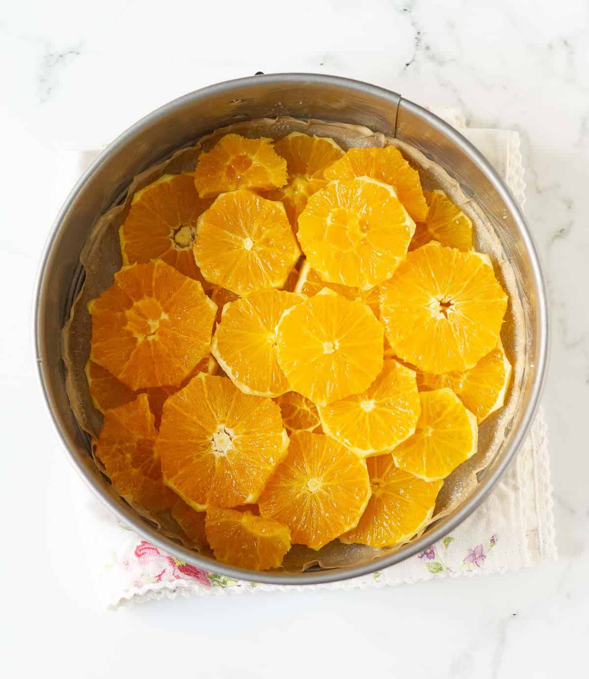 Peeled Orange slices arranged at the bottom of a cake pan.