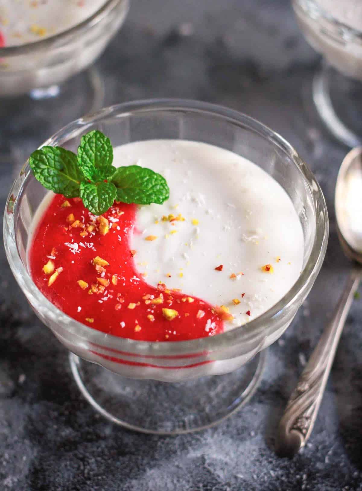A bowl of coconut panna cotta with strawberry sauce and a sprig of mint.