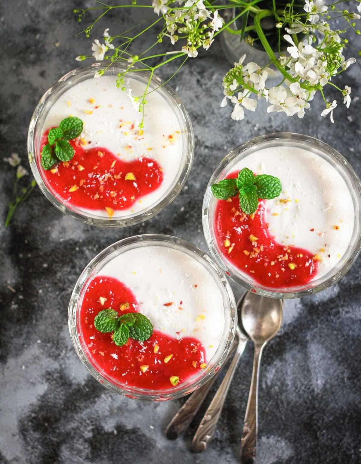 3 bowls of panna cotta with strawberry sauce on top.