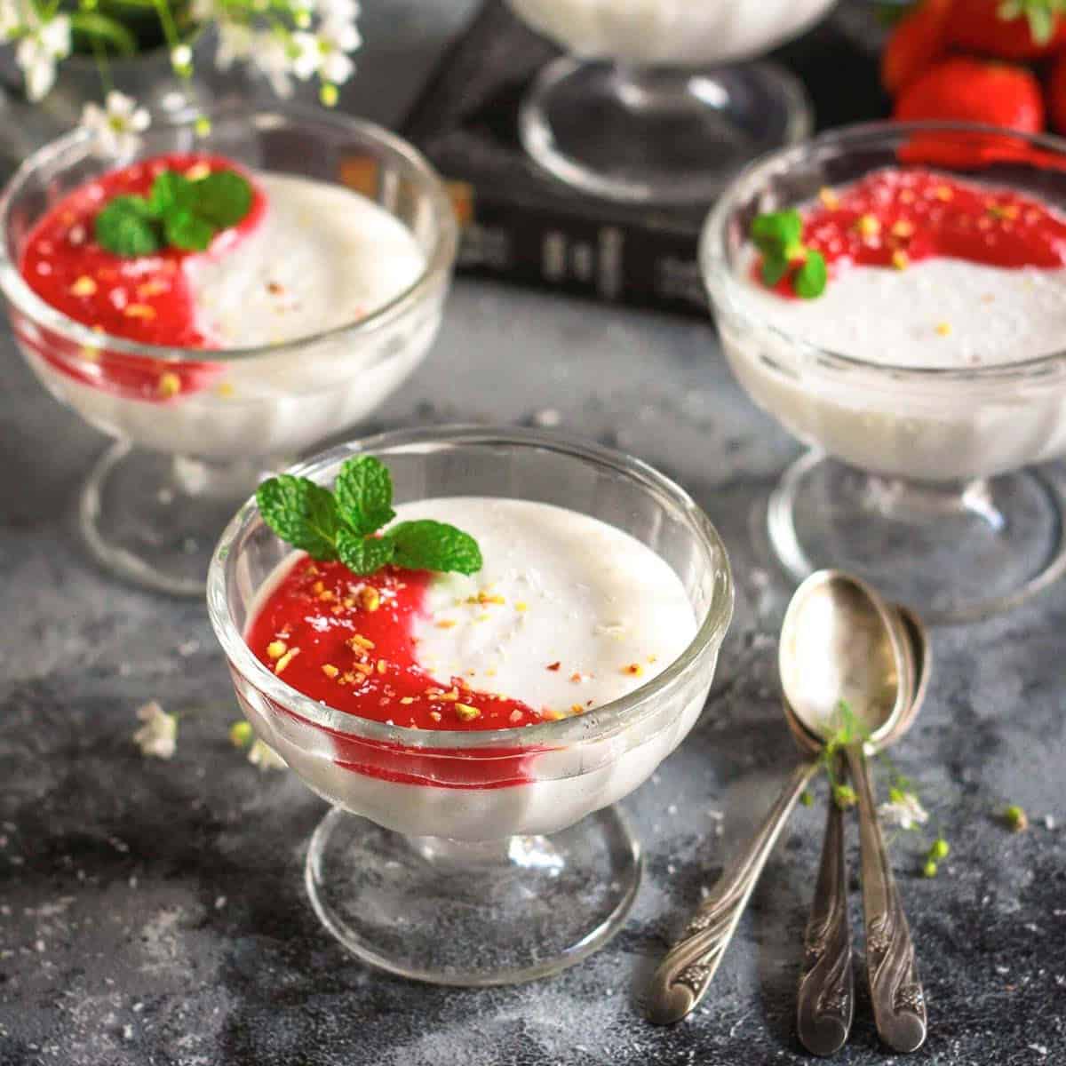 coconut panna cotta in glass bowls with strawberry sauce on top.