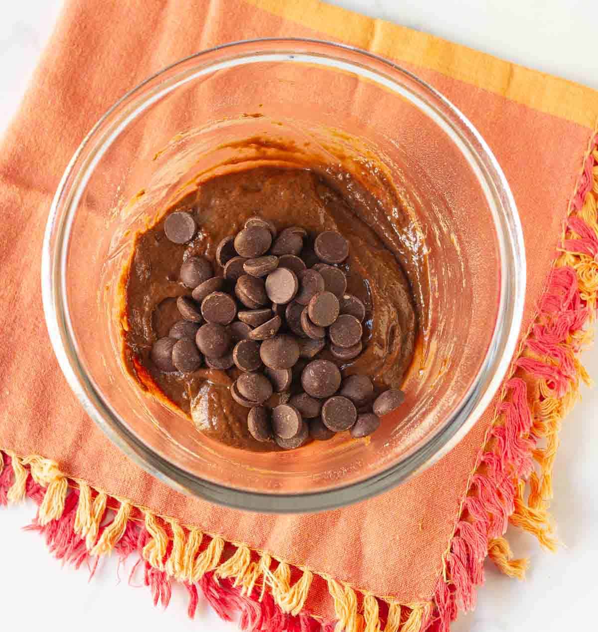 chocolate chips on top of brownie batter in a bowl.
