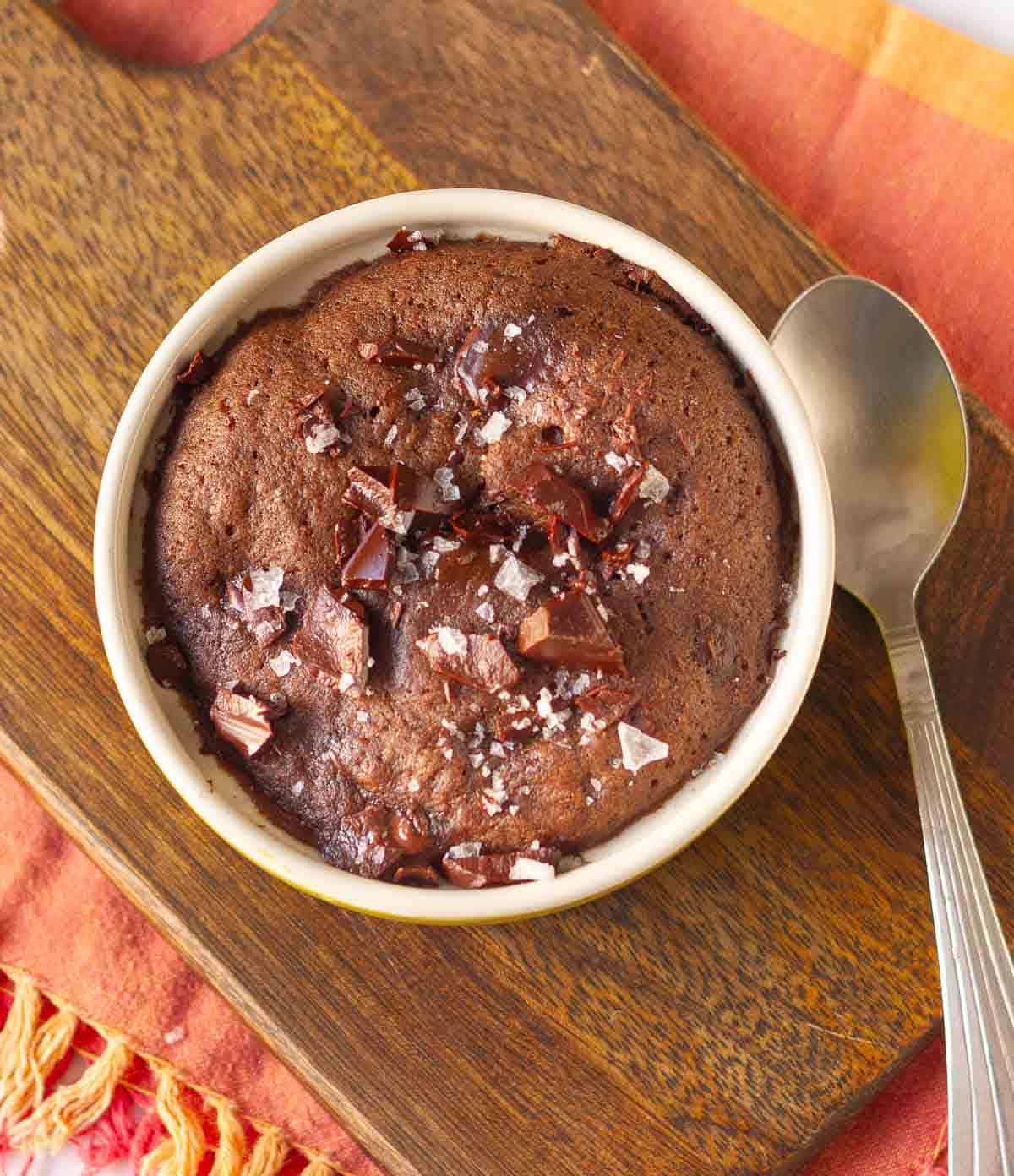 Baked brownie in a ramekin on a wooden board with a spoon.