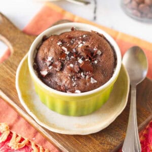 brownie mug cake in a green ramekin on a small plate and wooden board.