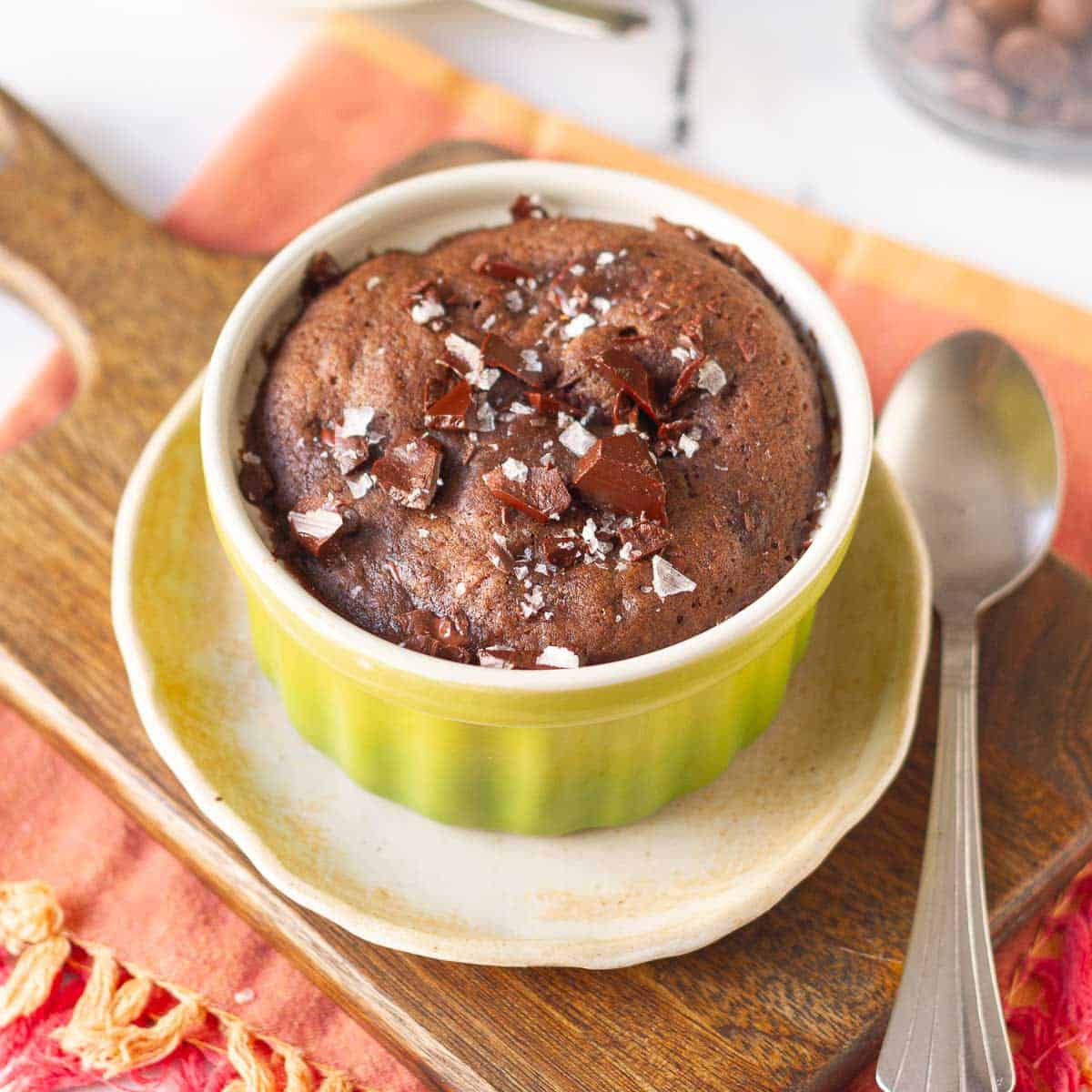 brownie mug cake in a green ramekin on a small plate and wooden board.
