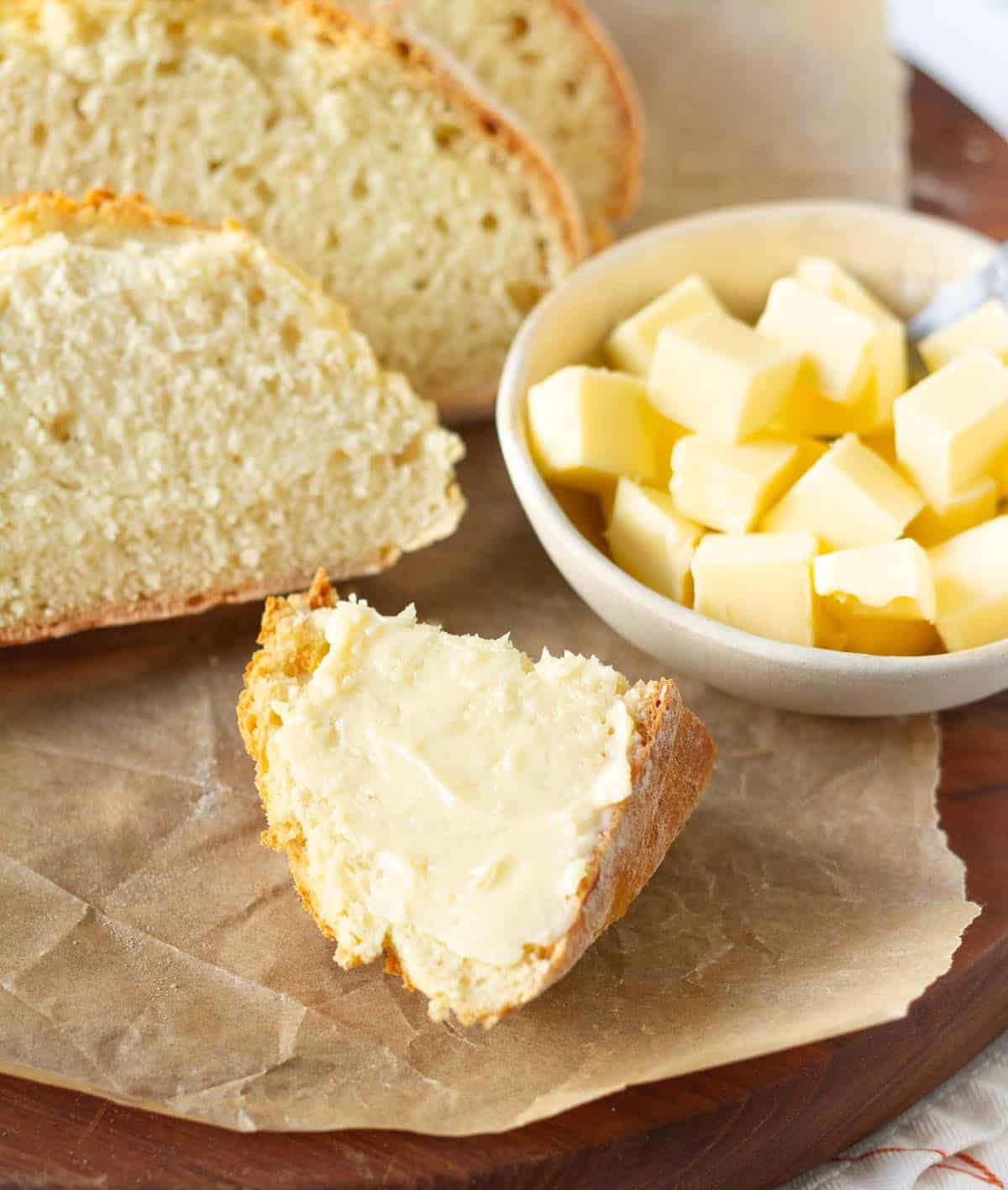 A buttered slice of bread with a bowl of butter and bread slices.