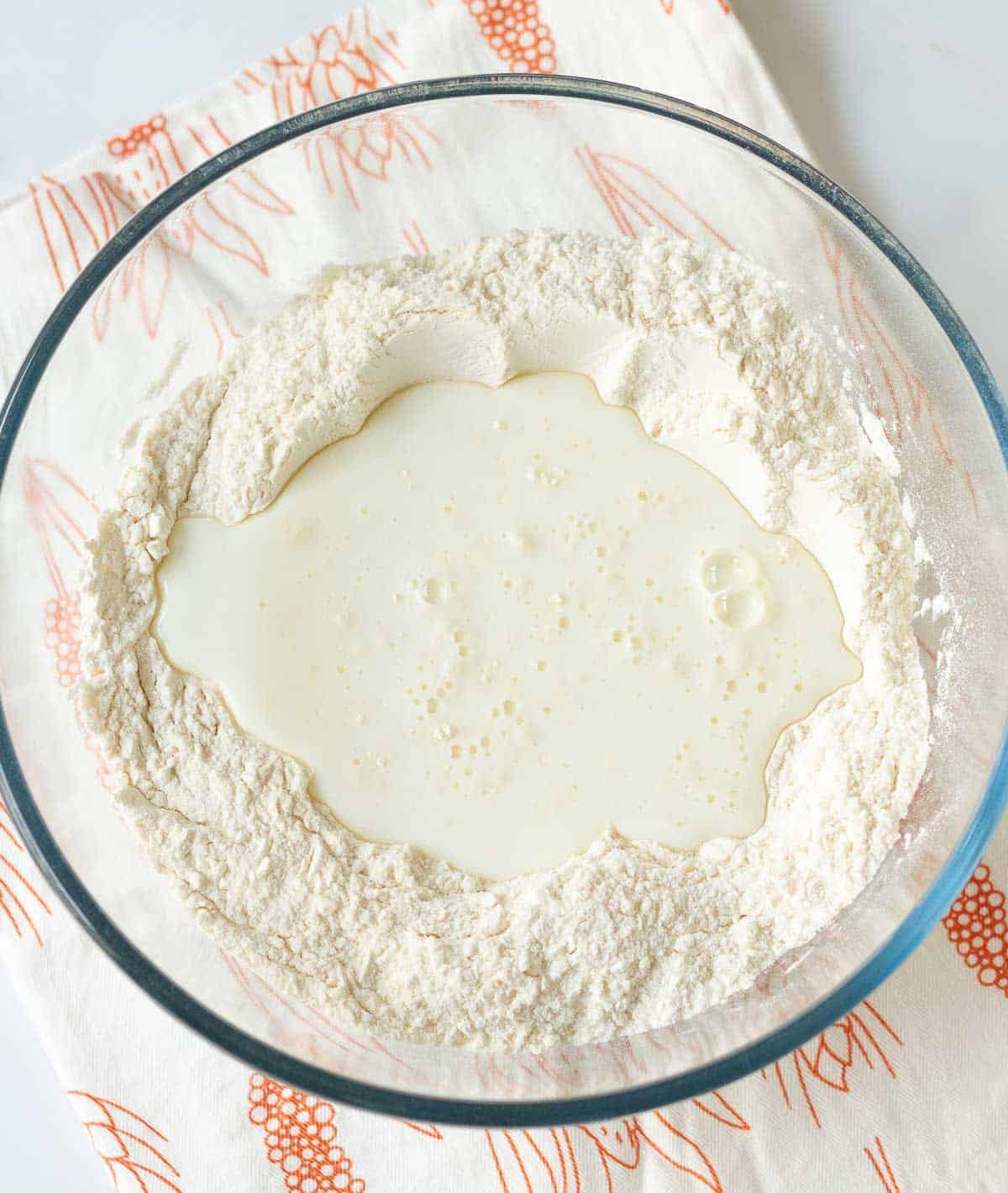 Buttermilk on top of the dry ingredients for making bread in a bowl.