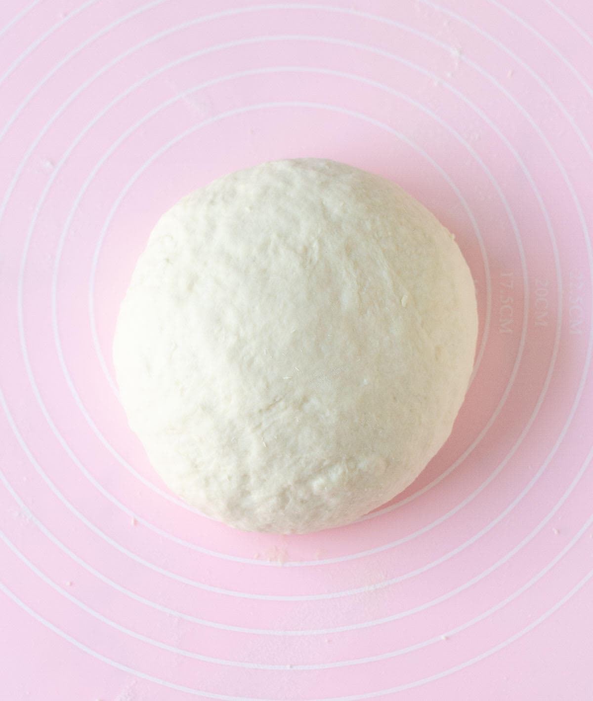 Smooth, kneaded bread dough on a pink silicone mat.