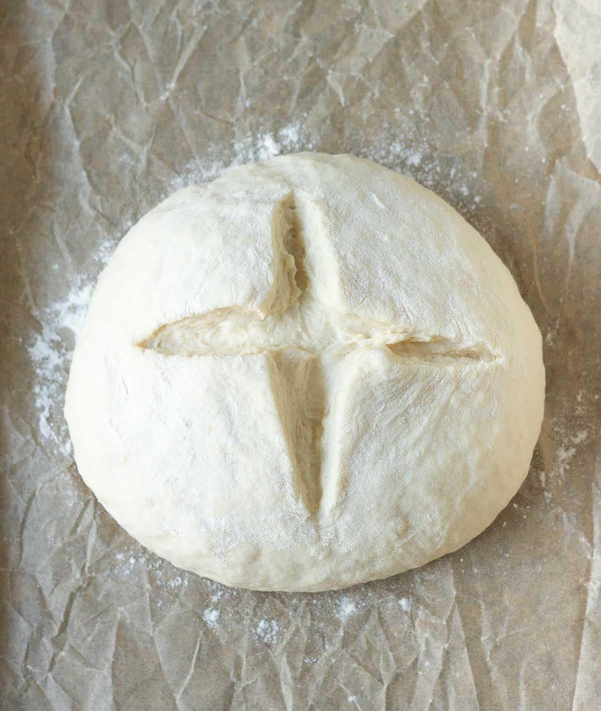 Bread dough marked with a cross on parchment paper.