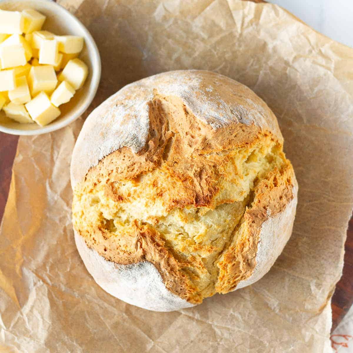 Loaf of bread with a bowl of butter on parchment paper.
