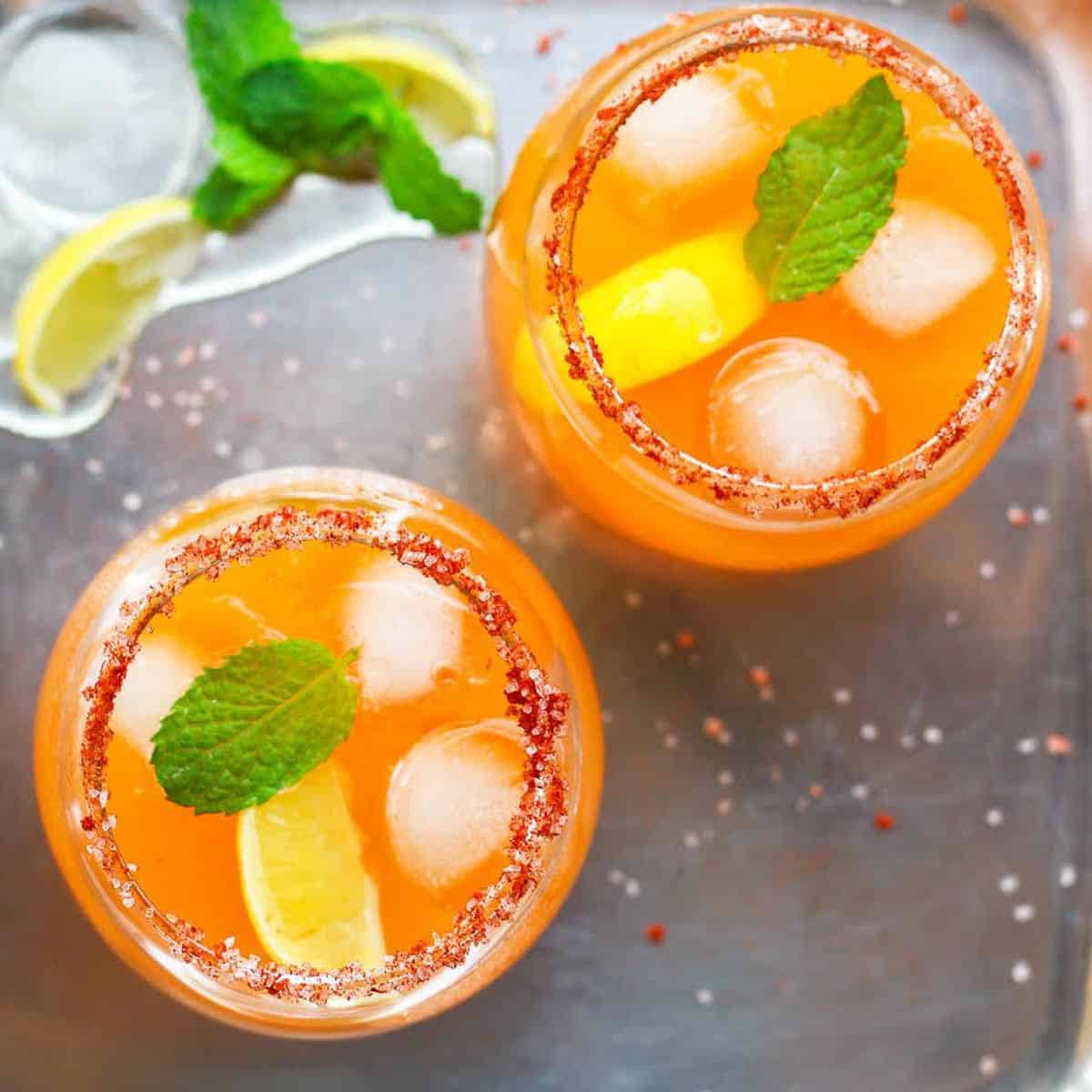 2 glasses of mango margarita with ice, lemon, and mint.